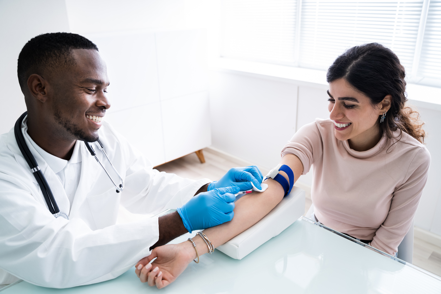 A male doctor performs a blood draw on a female patient.