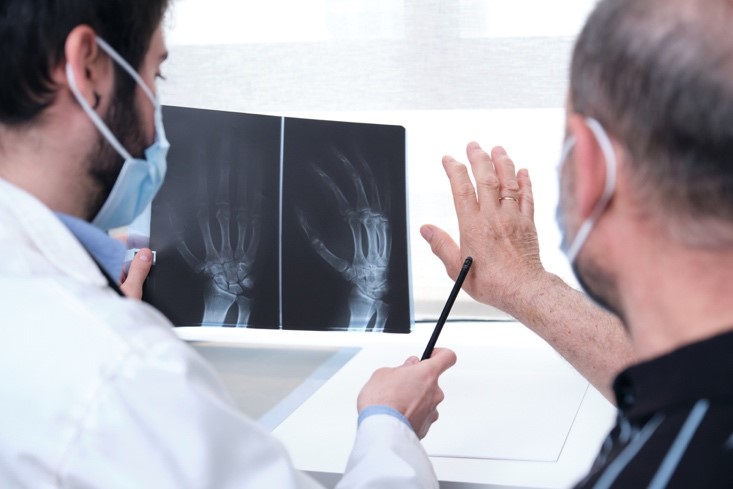 A doctor points to a patient’s hand and reviews a hand X-ray of the patient in a doctor’s office.