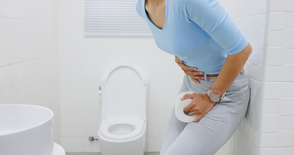 A closeup of a woman holding a roll of toilet paper with a hand on her torso standing in the bathroom.
