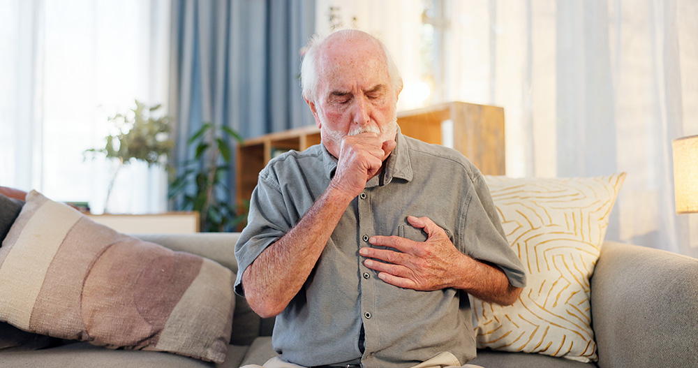 An older man coughs while clutching his chest
