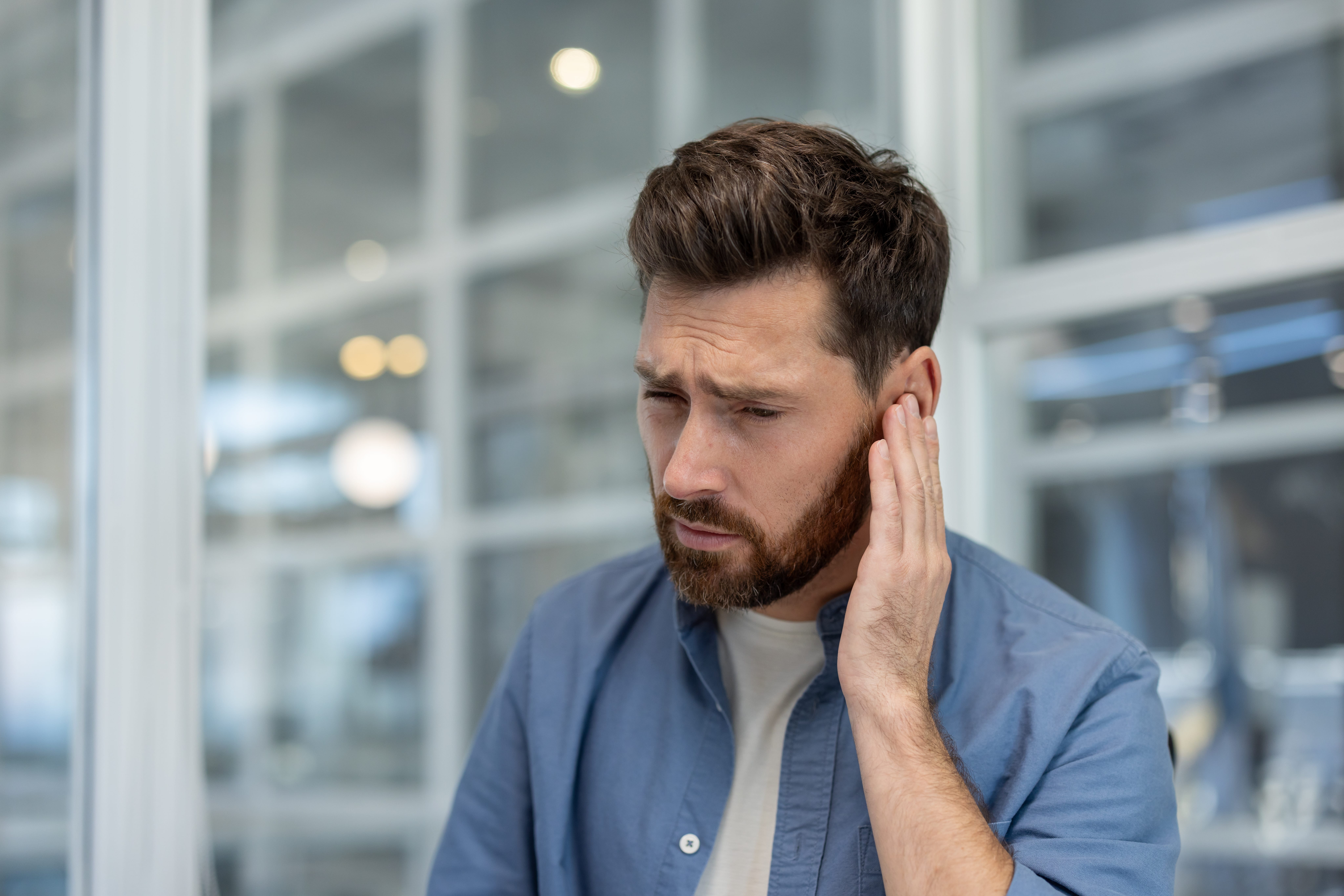 Man holding hand to ear, appearing to experience discomfort from earache, tinnitus, or hearing problem.