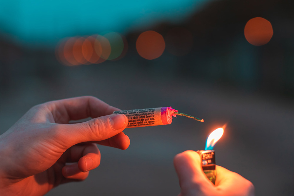 Person holding unlit firecracker outdoors at dusk with a closeup of hand with sparking pyrotechnic device