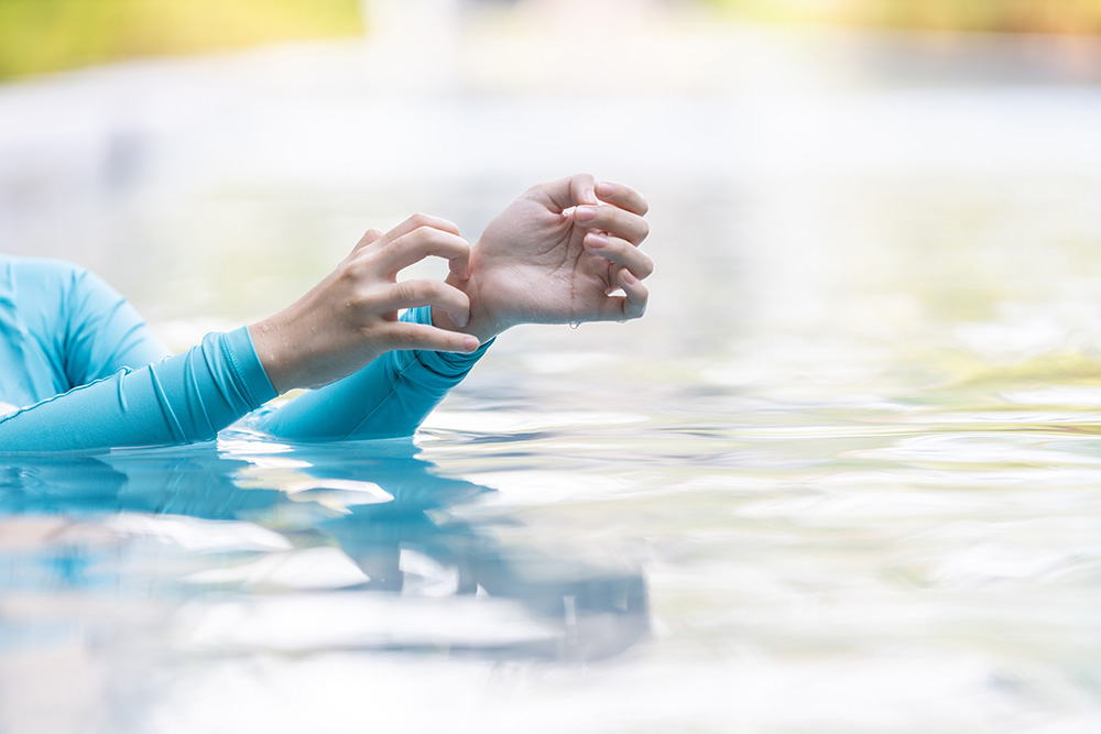 Girl in a pool scratching her itchy arms.